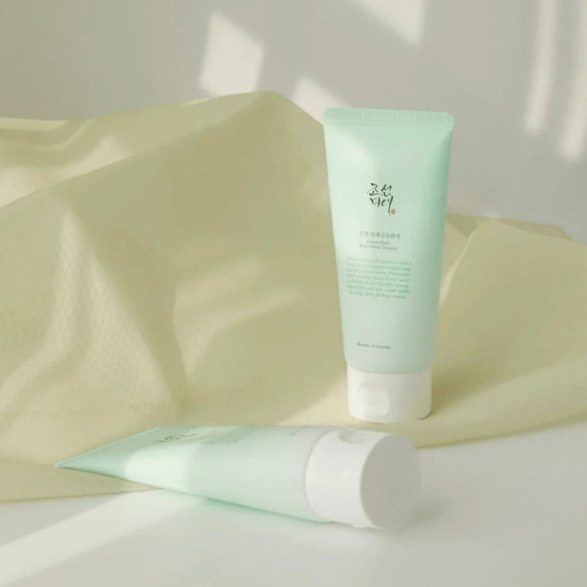 Beauty of Joseon Green Plum Refreshing Cleanser tube on fabric background – Mild low pH Korean face cleanser that soothes and balances skin with natural plum water.