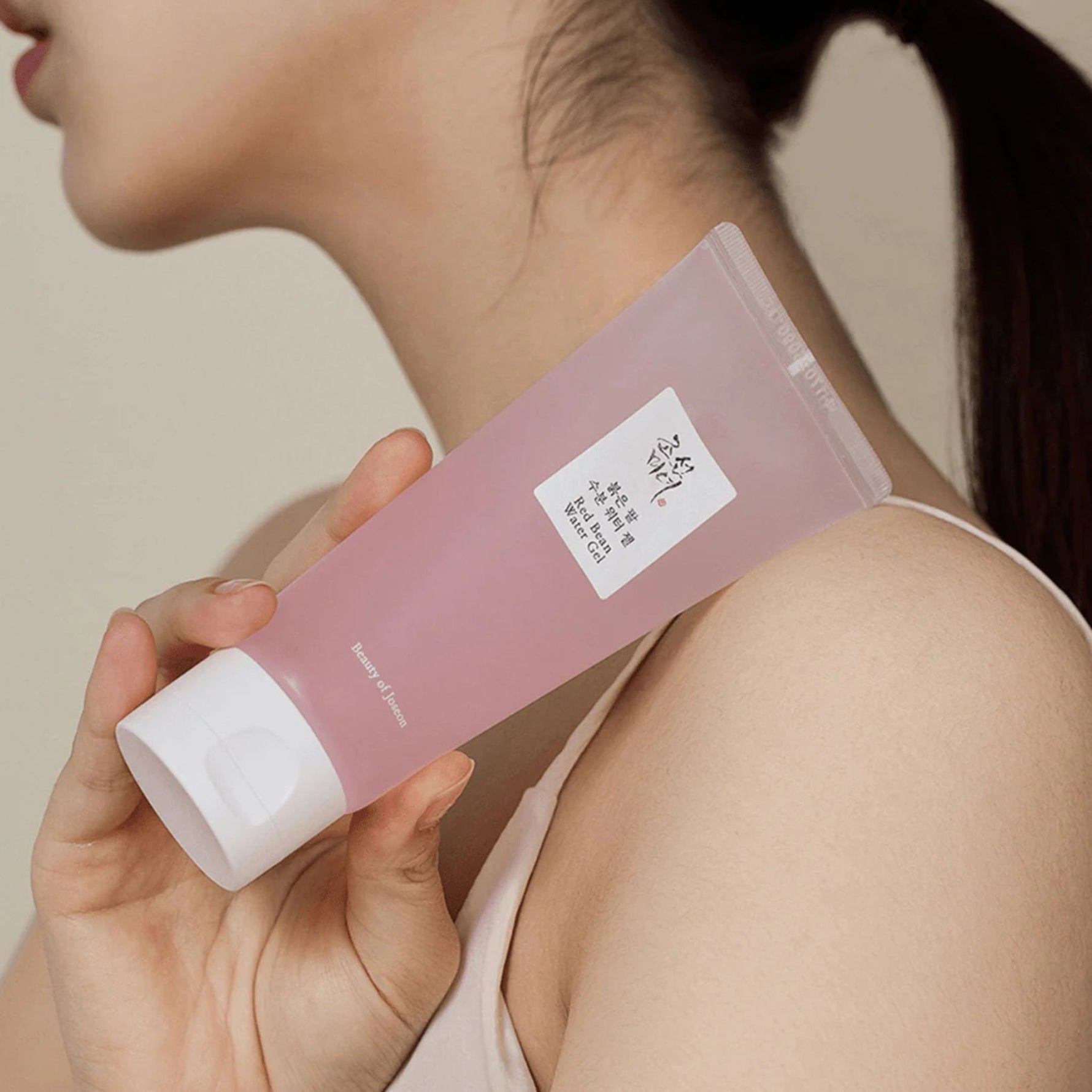 Model holding Beauty of Joseon Red Bean Water Gel pink tube against shoulder for skincare routine