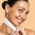 Woman smiling with dots of Celimax Pore + Dark Spot Brightening Cream on her face while holding the tube - K-beauty brightening cream
