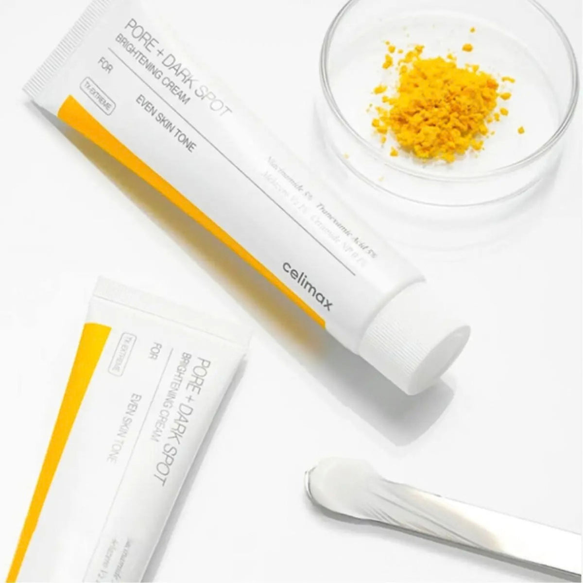 Celimax Pore + Dark Spot Brightening Cream tubes flat lay with yellow ingredient powder and a spatula of white cream