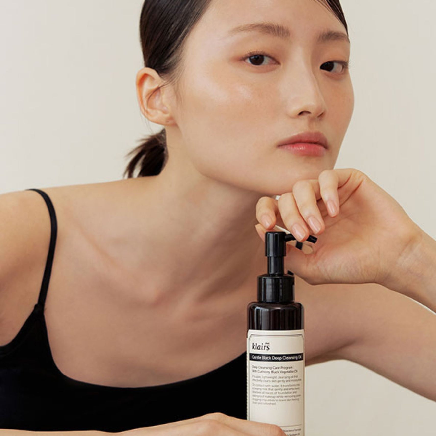Model with glowing skin posing beside Klairs Gentle Black Deep Cleansing Oil — deep cleansing care for soft, refreshed skin