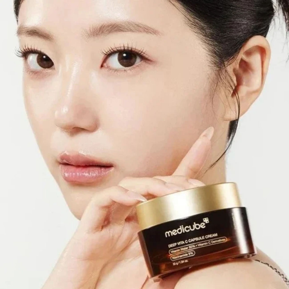 Model with glowing skin holding Medicube Deep Vita C Capsule Cream – K-beauty vitamin C cream for radiant, dewy skin