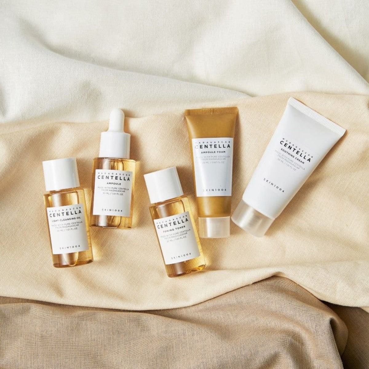 Skin1004 Madagascar Centella Travel Kit travel-size skincare set including ampoule, toner, cleansing oil, foam, and soothing cream on fabric