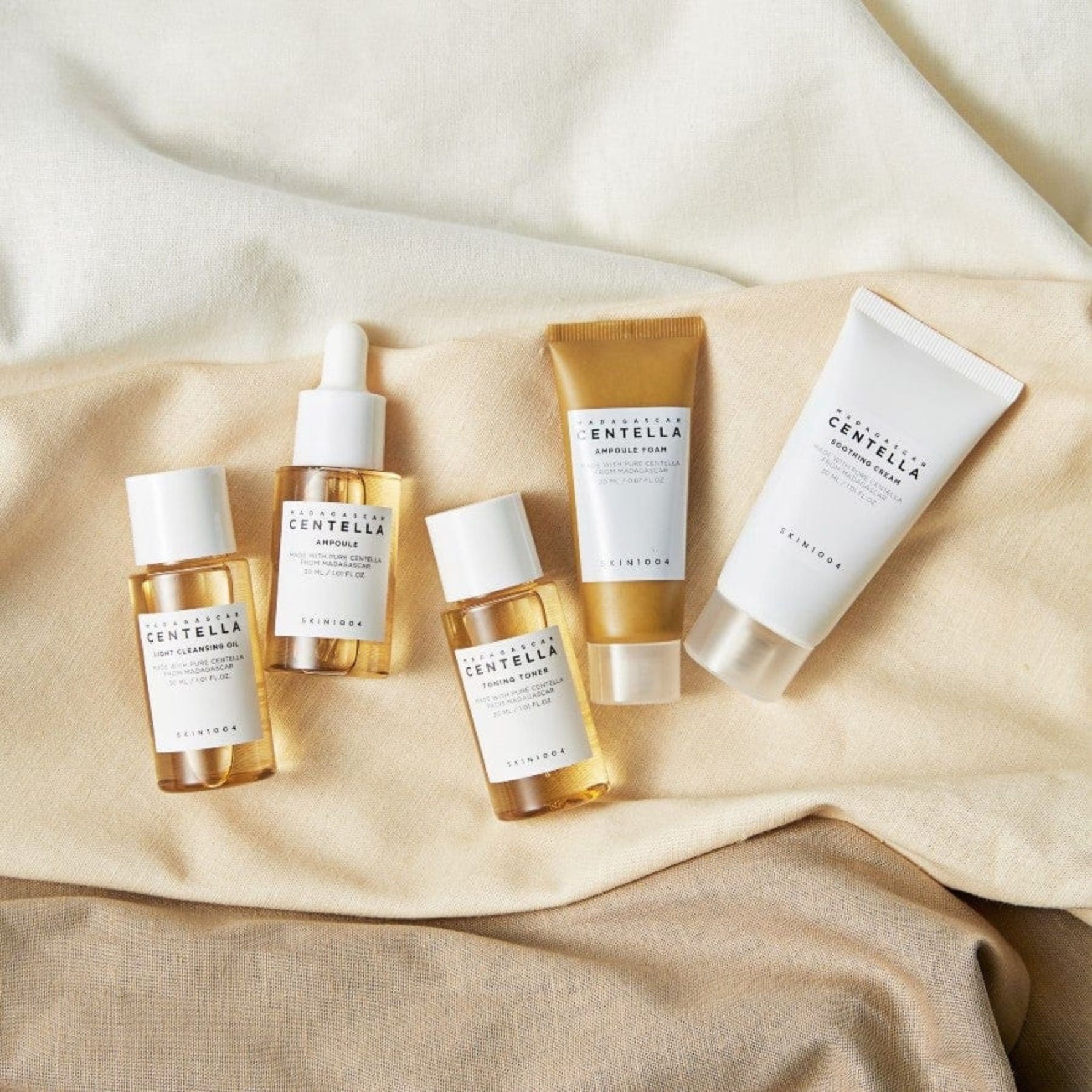 Skin1004 Madagascar Centella Travel Kit travel-size skincare set including ampoule, toner, cleansing oil, foam, and soothing cream on fabric