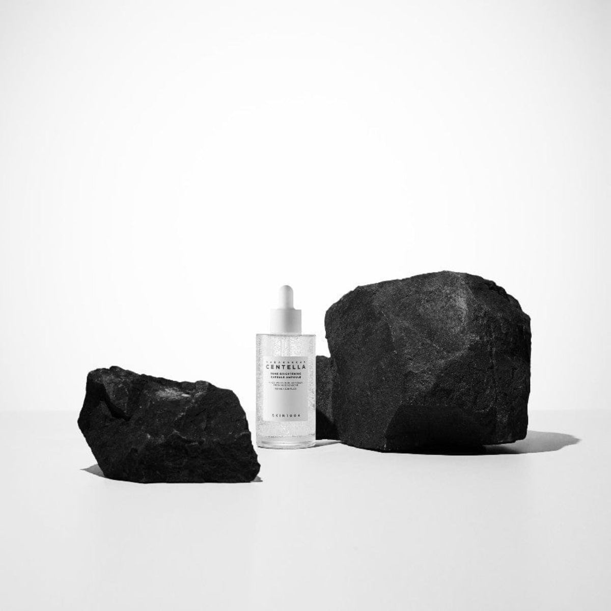 Skin1004 Madagascar Centella brightening ampoule serum bottle with black rocks minimalist skincare photography